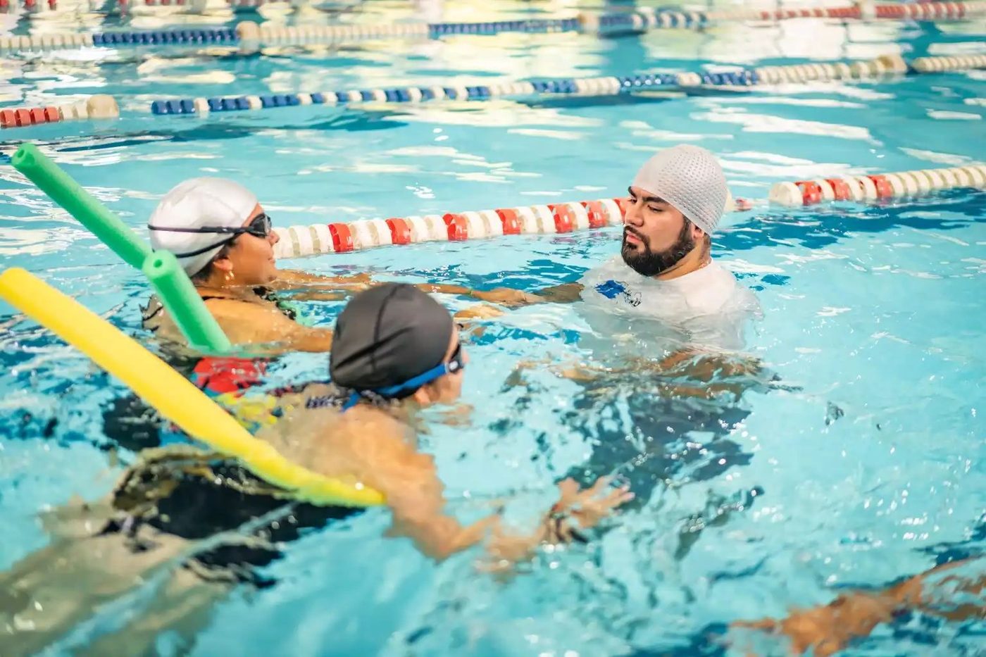 Instructor guiando a dos adultos en una clase de natación
